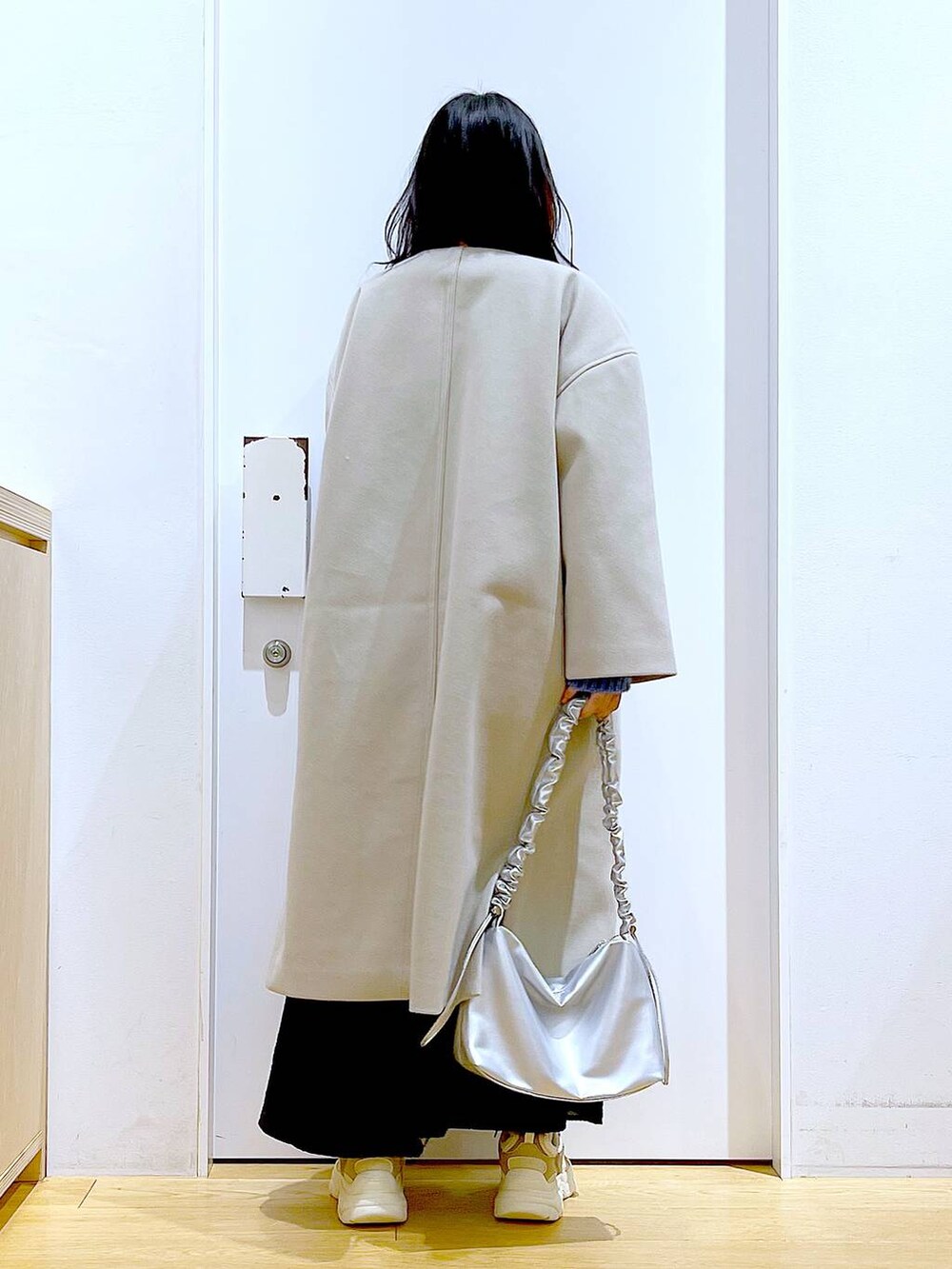 シルバー系のショルダーバッグ、ベージュ系のスニーカー、ベージュ系のノーカラーコートを着用したレディースの冬コーディネートの5枚目の写真