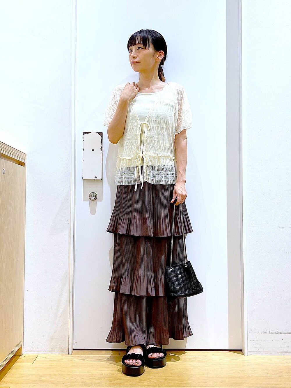 ブラウン系のスカート、ブラック系のサンダル、ホワイト系のカーディガン/ボレロを着用したレディースの夏コーディネートの2枚目の写真