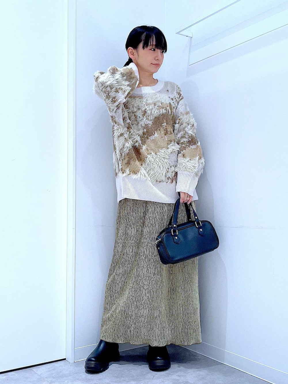 ブラック系のブーツ、ブラック系のショルダーバッグ、グリーン系のスカートを着用したレディースの冬コーディネートの2枚目の写真