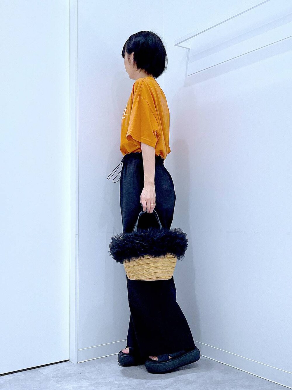 ベージュ系のショルダーバッグ、ブラック系のサンダル、オレンジ系のTシャツ/カットソーを着用したレディースの夏コーディネートの3枚目の写真