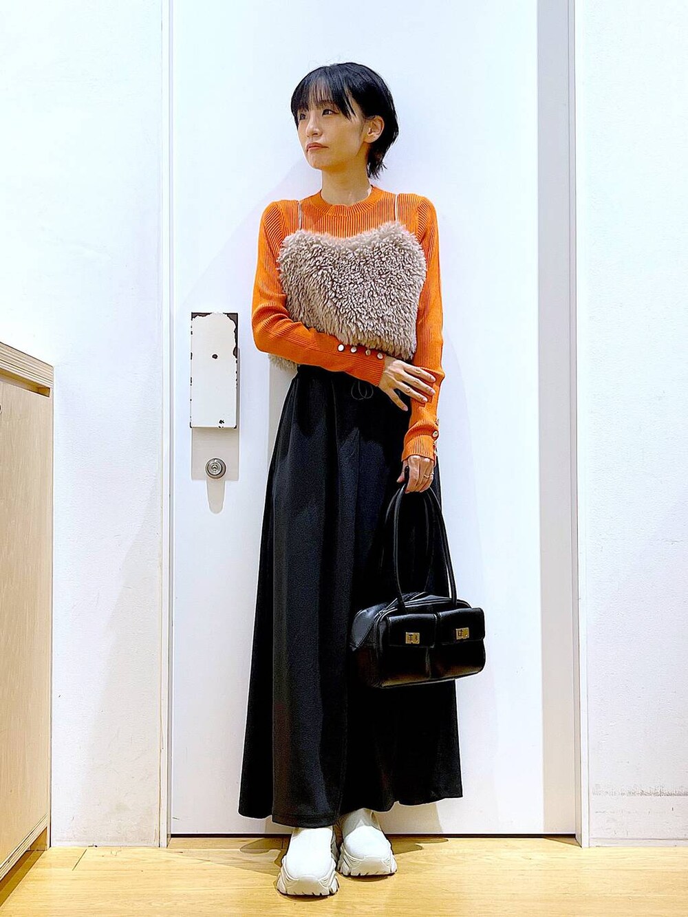 オレンジ系のニット/セーター、ブラウン系のベスト、ブラック系のハンドバッグを着用したレディースの秋コーディネートの2枚目の写真