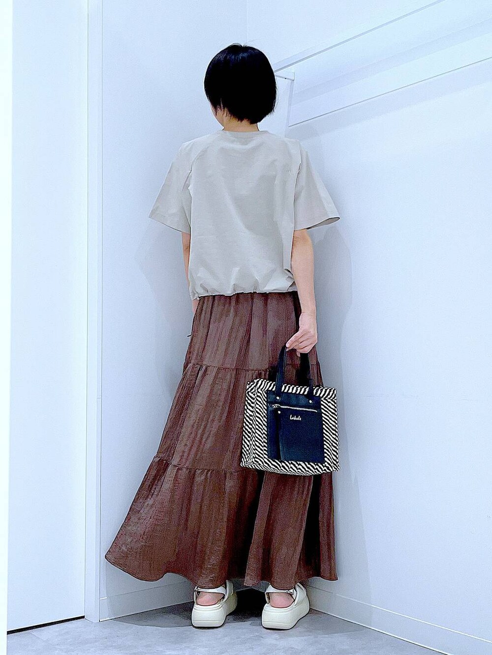 ブラック系のショルダーバッグ、ホワイト系のサンダル、ベージュ系のTシャツ/カットソーを着用したレディースの夏コーディネートの5枚目の写真