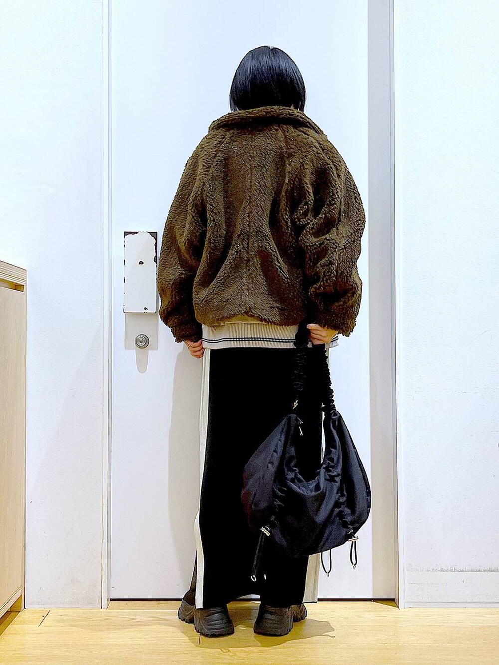 ブラック系のスカート、ブラック系のショルダーバッグ、ブラック系のブーツを着用したレディースの冬コーディネートの5枚目の写真