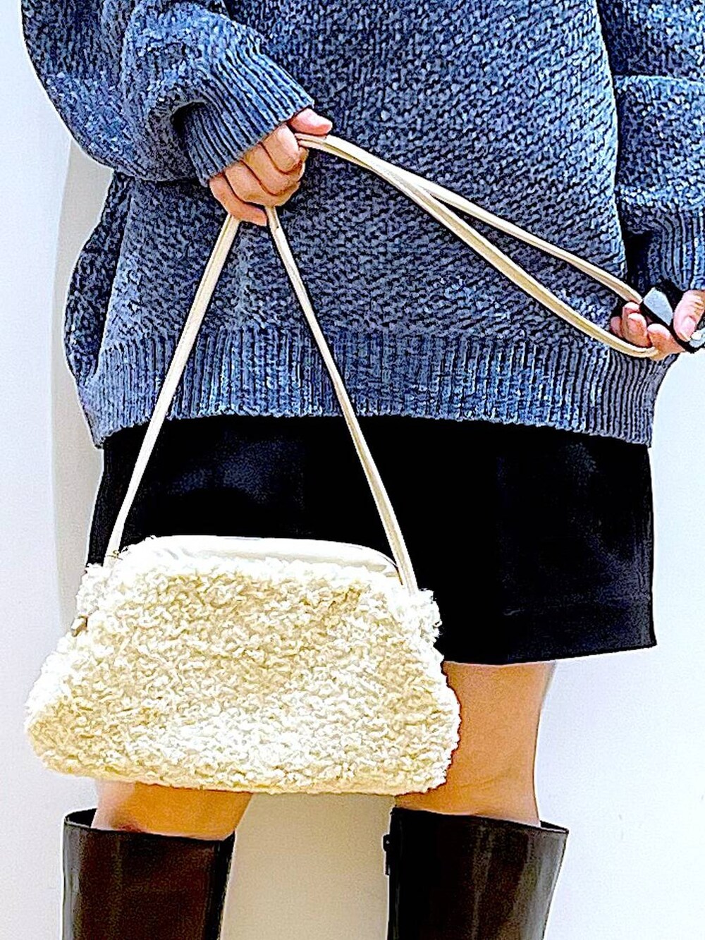 ブルー系のニット/セーター、ホワイト系のクラッチバッグ、ブラック系のブーツを着用したレディースの冬コーディネートの9枚目の写真