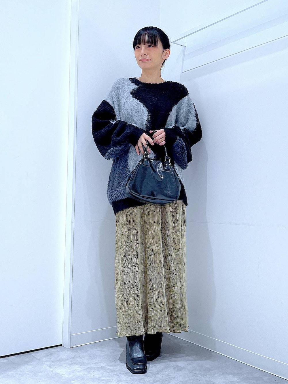 グレー系のニット/セーター、ブラック系のブーツ、ブラック系のショルダーバッグを着用したレディースの冬コーディネートの2枚目の写真