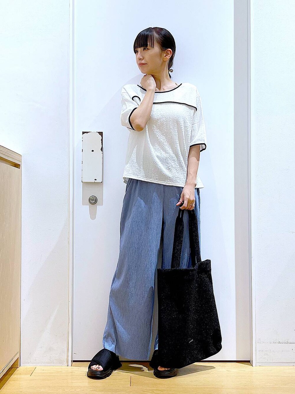 ブラック系のトートバッグ、ブラック系のサンダル、ホワイト系のTシャツ/カットソーを着用したレディースの夏コーディネートの2枚目の写真