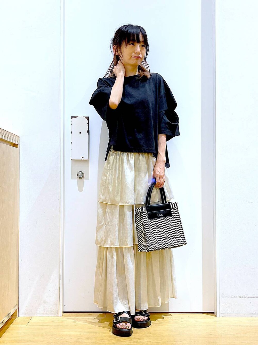 ブラック系のサンダル、ブラック系のショルダーバッグ、ゴールド系のスカートを着用したレディースの夏コーディネートの2枚目の写真