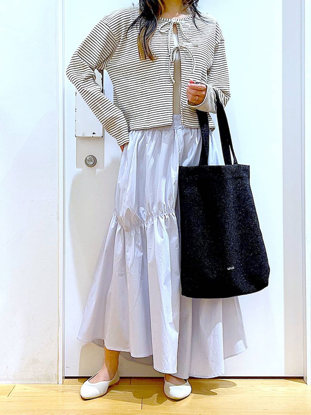 ブラック系のトートバッグ、ブルー系のスカート、イエロー系のニット/セーターを着用したレディースの春コーディネートの6枚目の写真