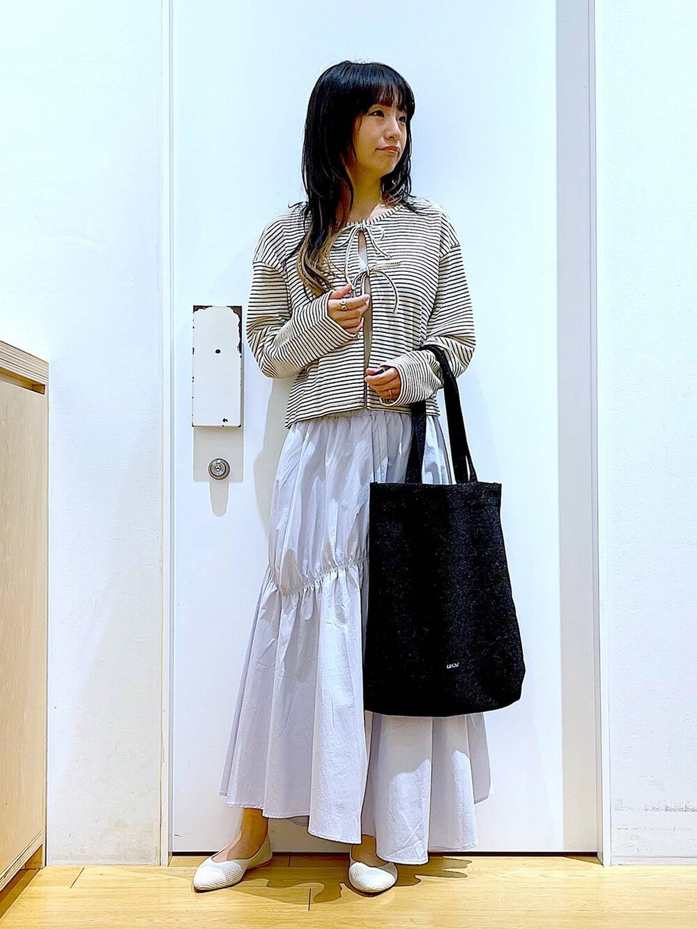 ブラック系のトートバッグ、ブルー系のスカート、イエロー系のニット/セーターを着用したレディースの春コーディネートの2枚目の写真