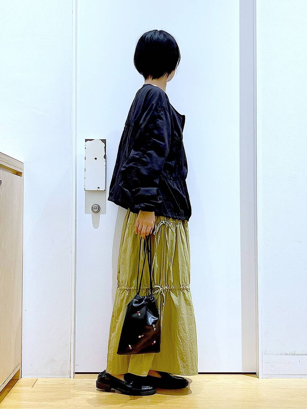 ブラック系のショルダーバッグ、ブラック系のローファー、イエロー系のスカートを着用したレディースの秋コーディネートの4枚目の写真