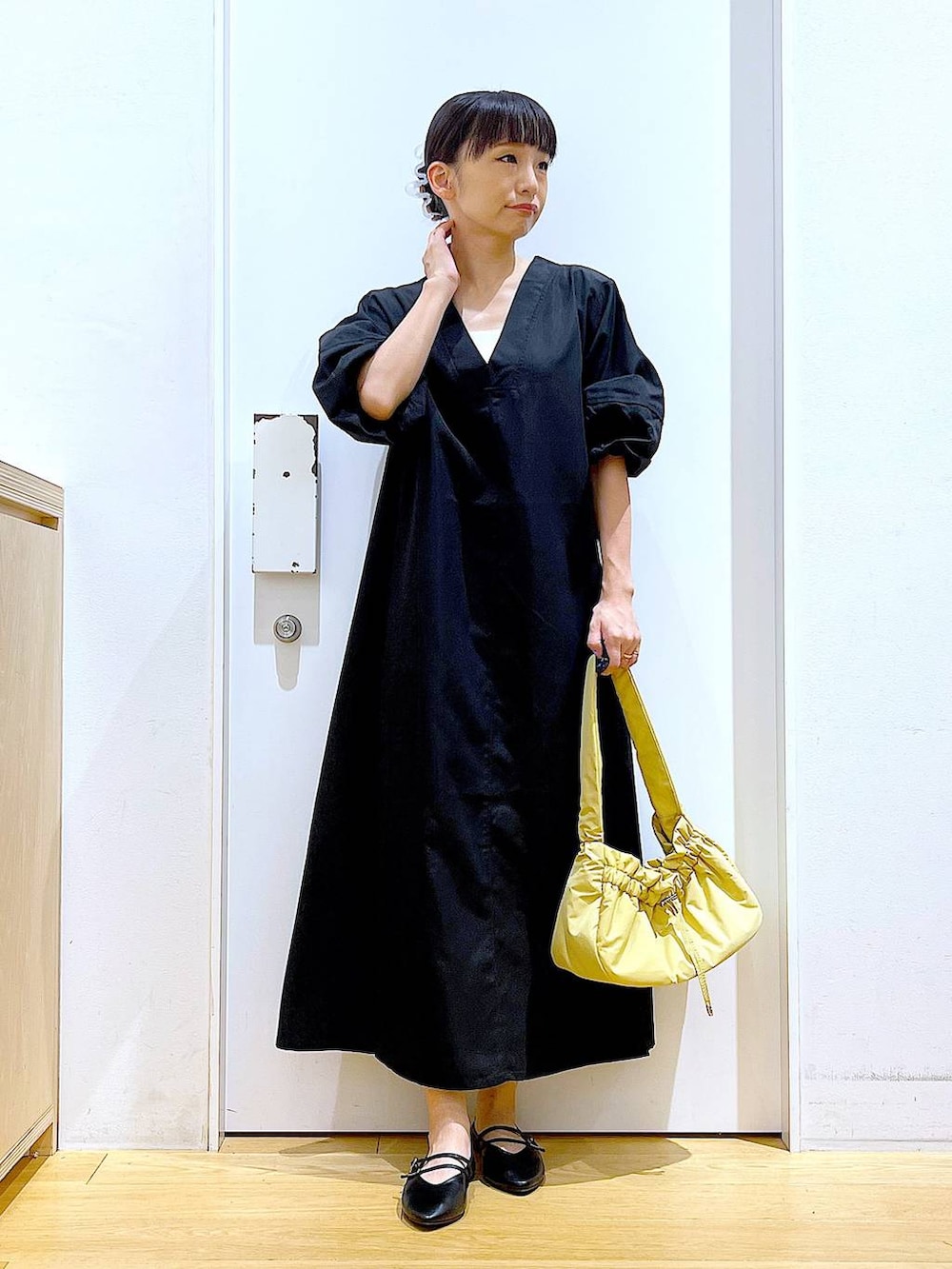 イエロー系のハンドバッグ、ブラック系のワンピース、ブラック系のパンプスを着用したレディースの秋コーディネートの2枚目の写真