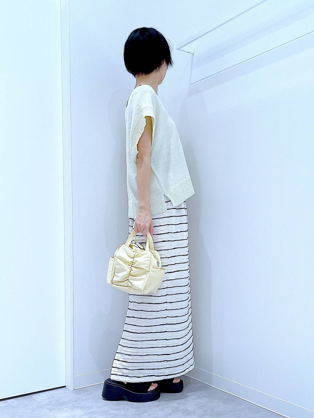 ブラック系のサンダル、イエロー系のショルダーバッグ、ホワイト系のスカートを着用したレディースの夏コーディネートの4枚目の写真