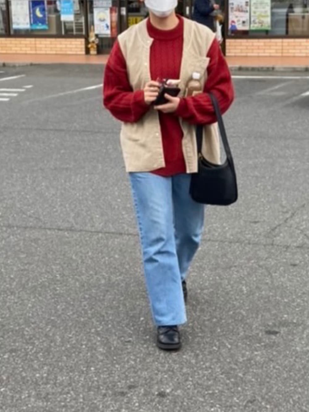 レッド系のニット/セーター、ベージュ系のベスト、ブルー系のデニムパンツを着用したレディースの冬コーディネートの2枚目の写真