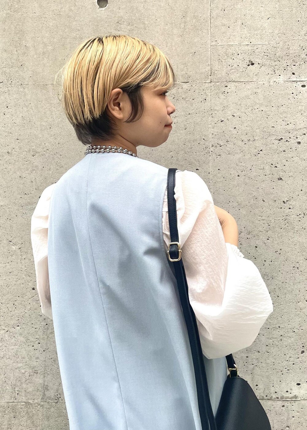 ブラック系のパンプス、ブラック系のショルダーバッグ、ブルー系のジャンパースカートを着用したレディースの春コーディネートの4枚目の写真