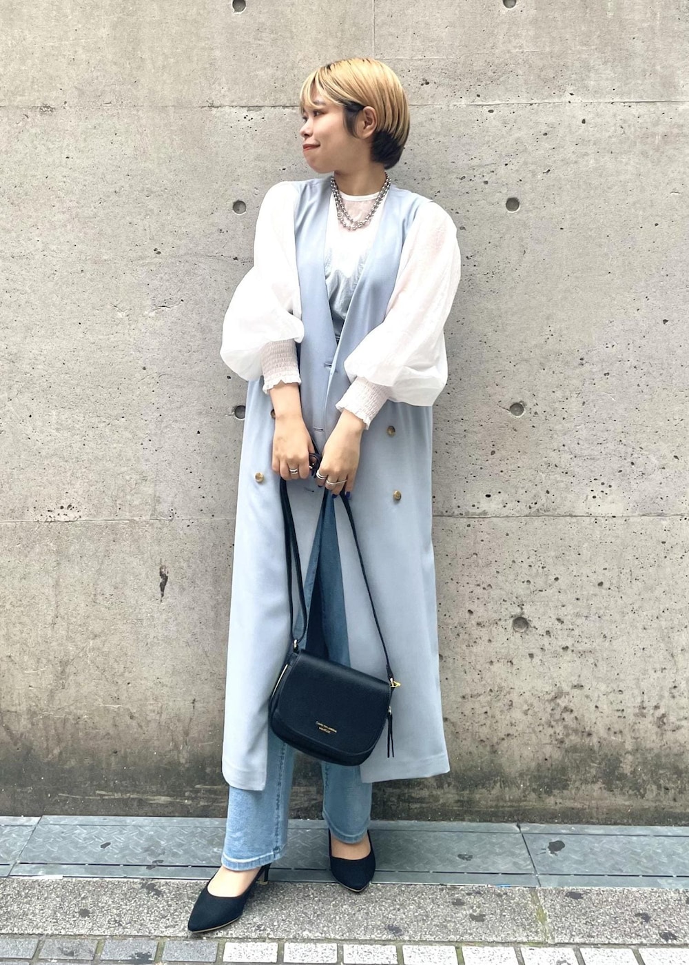 ブラック系のパンプス、ブラック系のショルダーバッグ、ブルー系のジャンパースカートを着用したレディースの春コーディネートの2枚目の写真
