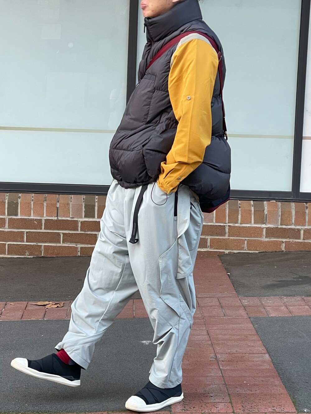グレー系のダウンベスト、ホワイト系のチノパンツ、ブラック系のスリッポンを着用したメンズの春コーディネートの2枚目の写真