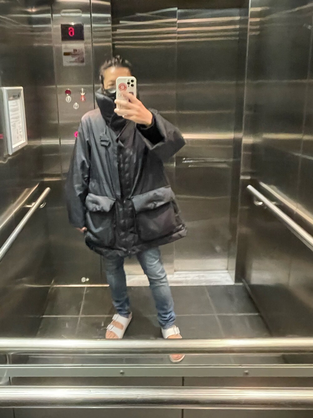 ブラック系のダウンベスト、ブルー系のデニムパンツ、ブラック系のサンダルを着用したメンズの春コーディネートの3枚目の写真