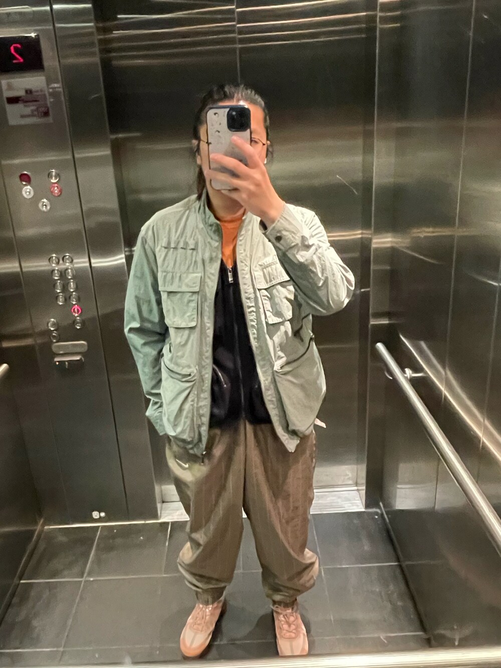 グリーン系のカーゴパンツ、ブラウン系のチノパンツ、オレンジ系のスニーカーを着用したメンズの春コーディネートの2枚目の写真