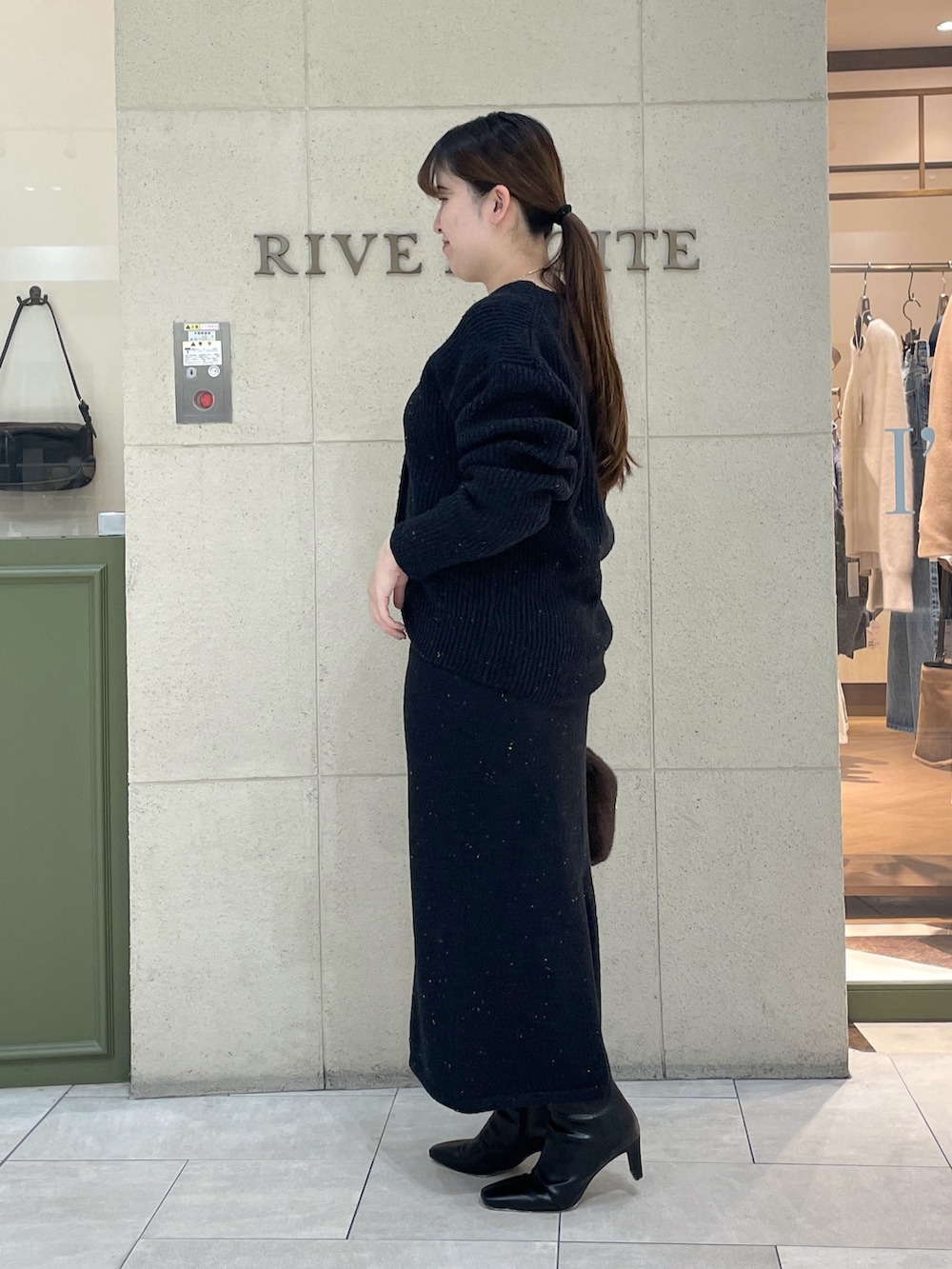 ブラック系のカーディガン/ボレロ、ブラック系のスカート、ブラウン系のボストンバッグを着用したレディースの秋コーディネートの3枚目の写真