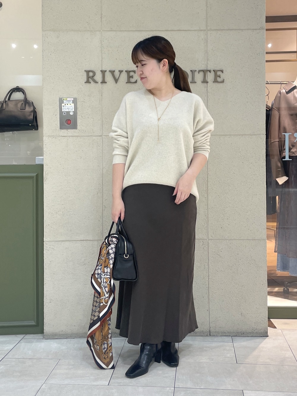 ベージュ系のニット/セーター、ブラウン系のスカート、ブラック系のボストンバッグを着用したレディースの秋コーディネートの2枚目の写真