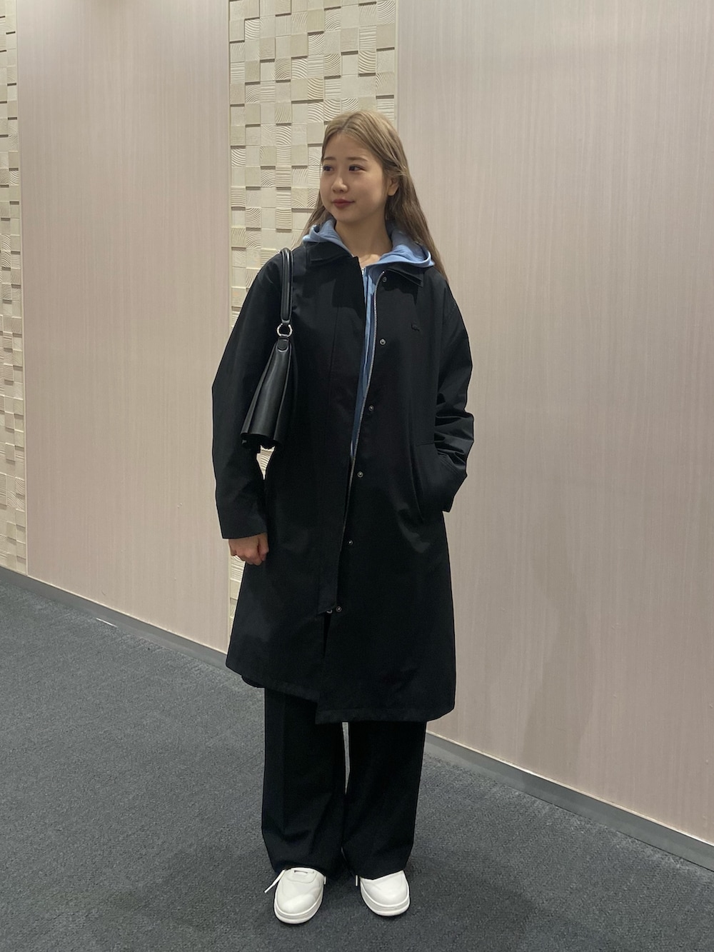 ブルー系のパーカー、ブラック系のステンカラーコート、ブラック系のスラックスを着用したレディースの冬コーディネートの3枚目の写真