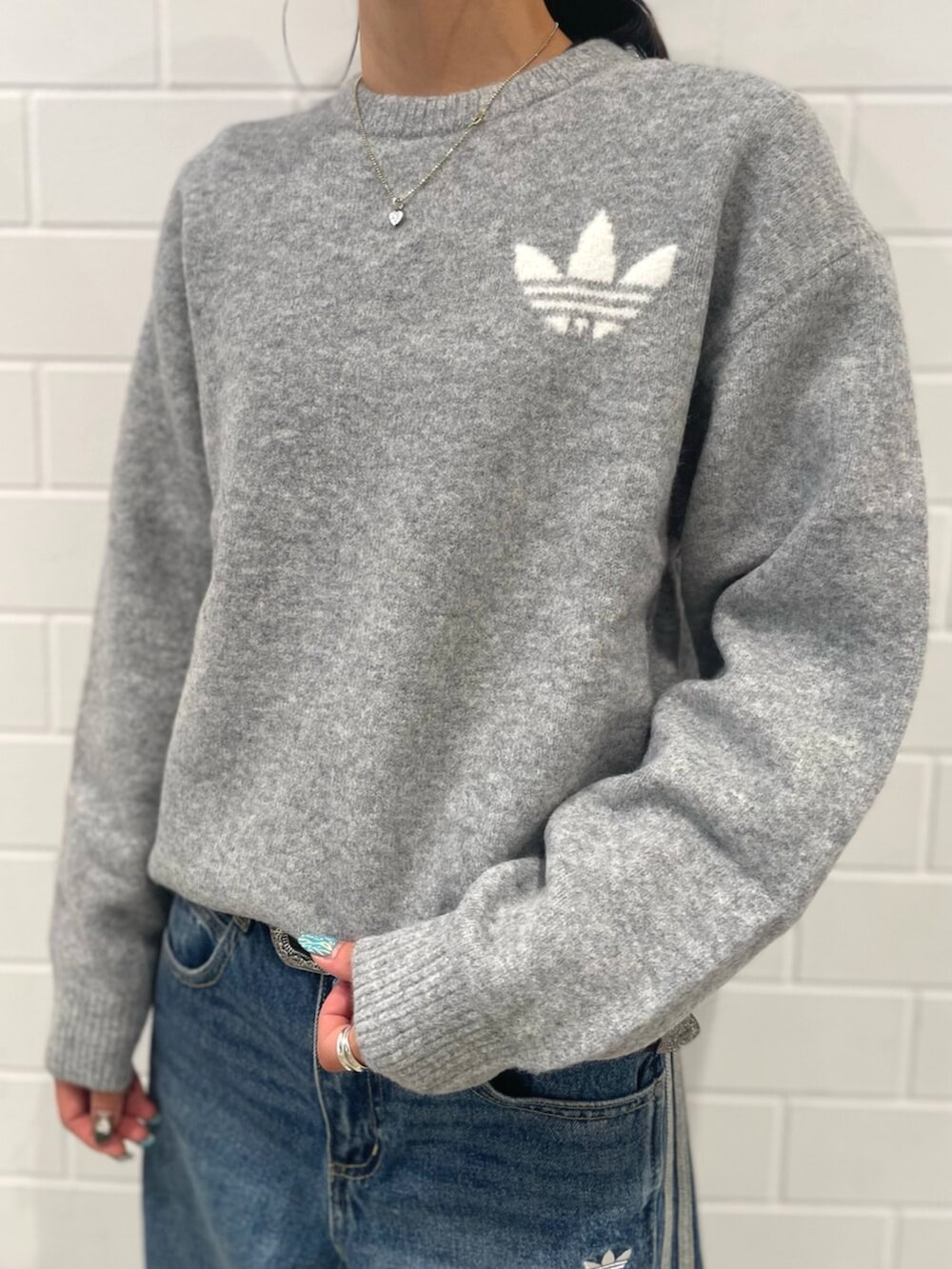 シルバー系のスニーカー、ブルー系のデニムパンツ、グレー系のニット/セーターを着用したレディースの秋コーディネートの4枚目の写真