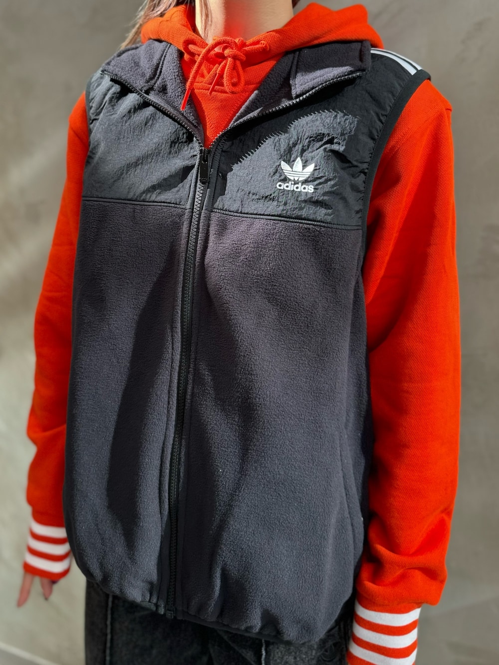 ブラック系のベスト、オレンジ系のパーカー、ブラック系のデニムパンツを着用したレディースの秋コーディネートの3枚目の写真