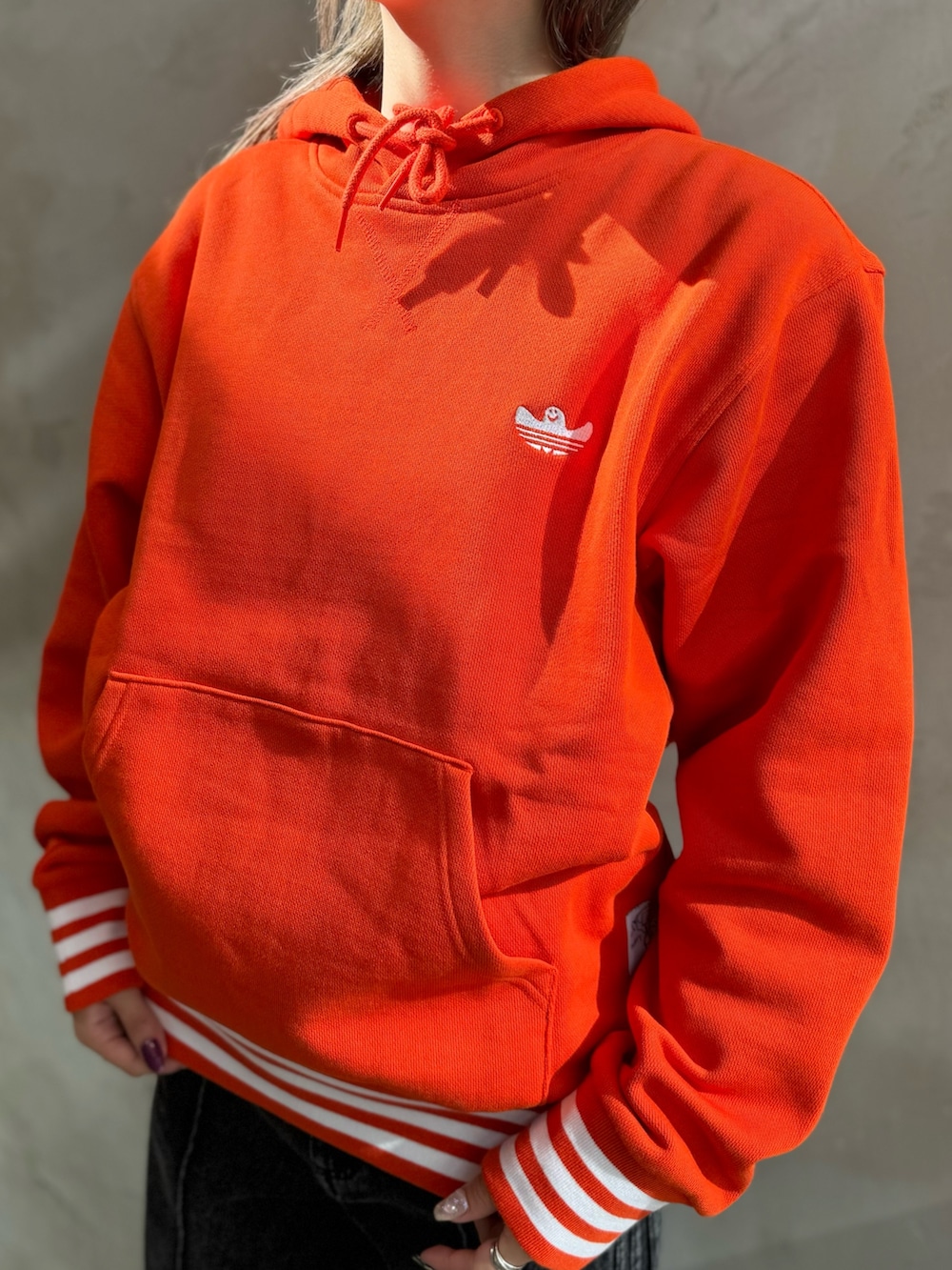 ブラック系のベスト、オレンジ系のパーカー、ブラック系のデニムパンツを着用したレディースの秋コーディネートの4枚目の写真