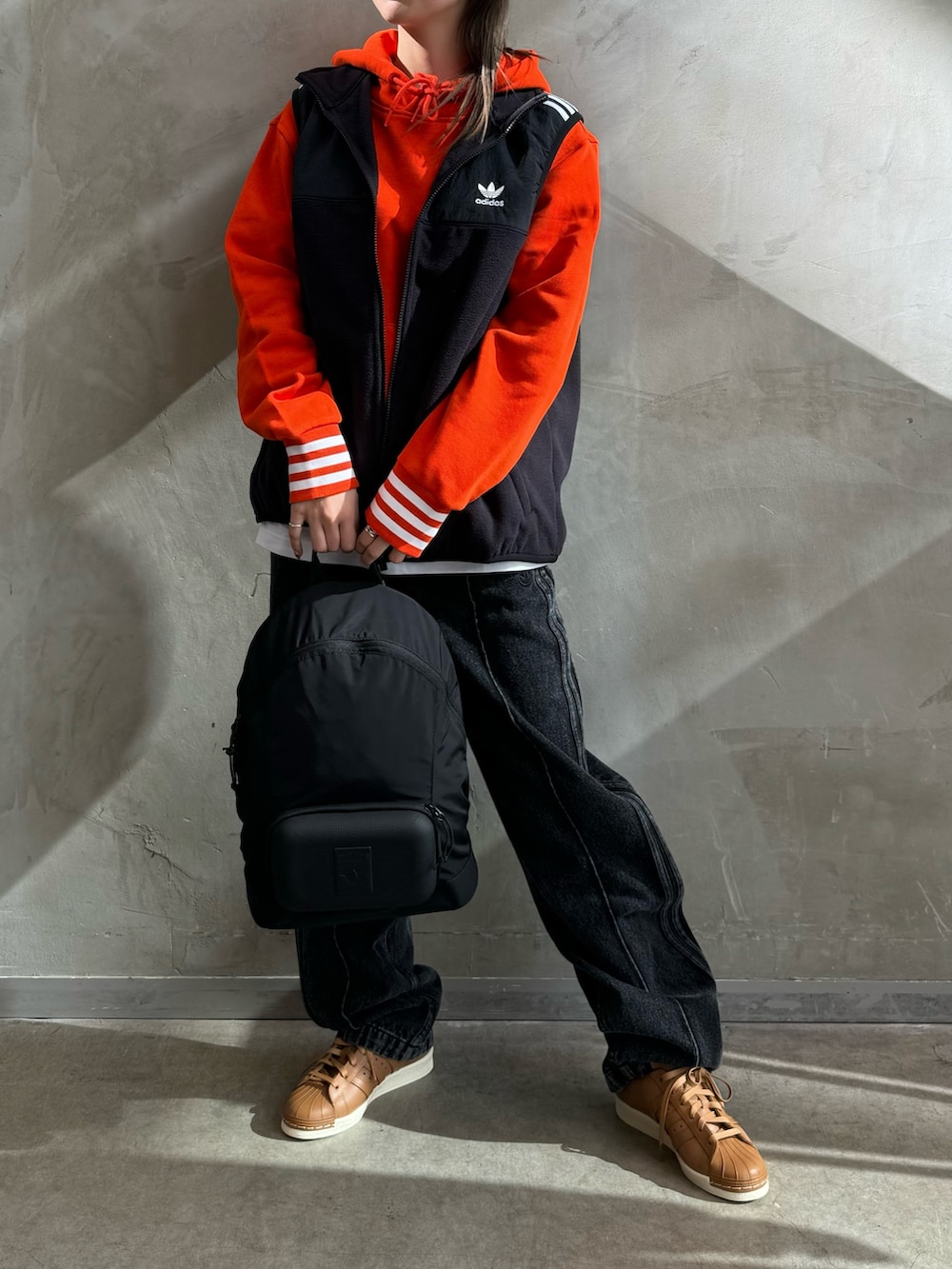 ブラック系のベスト、オレンジ系のパーカー、ブラック系のデニムパンツを着用したレディースの秋コーディネートの2枚目の写真