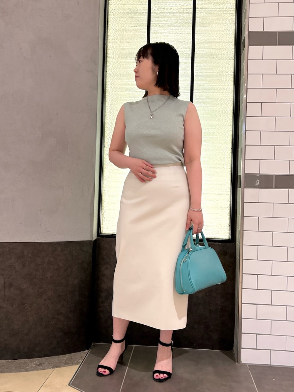グリーン系のニット/セーター、ホワイト系のスカート、グリーン系のボストンバッグを着用したレディースの夏コーディネートの5枚目の写真