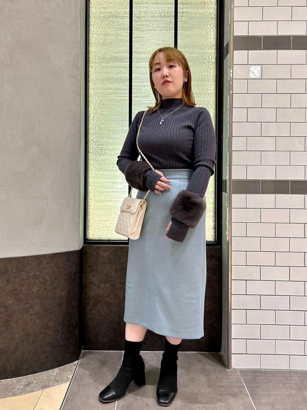 グレー系のニット/セーター、ブルー系のスカート、ホワイト系のショルダーバッグを着用したレディースの冬コーディネートの2枚目の写真