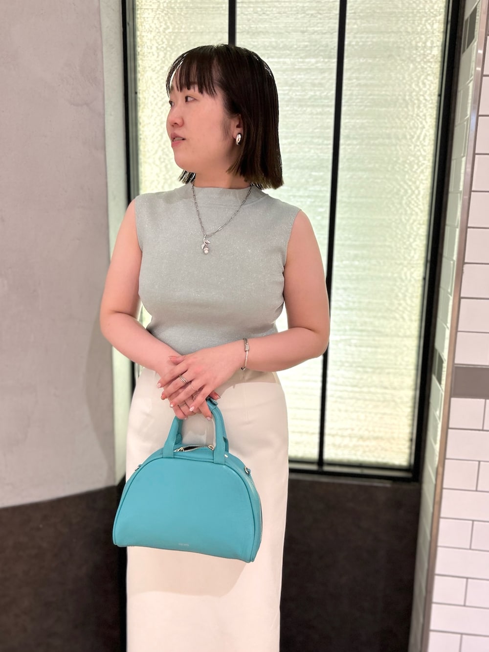 グリーン系のニット/セーター、ホワイト系のスカート、グリーン系のボストンバッグを着用したレディースの夏コーディネートの10枚目の写真