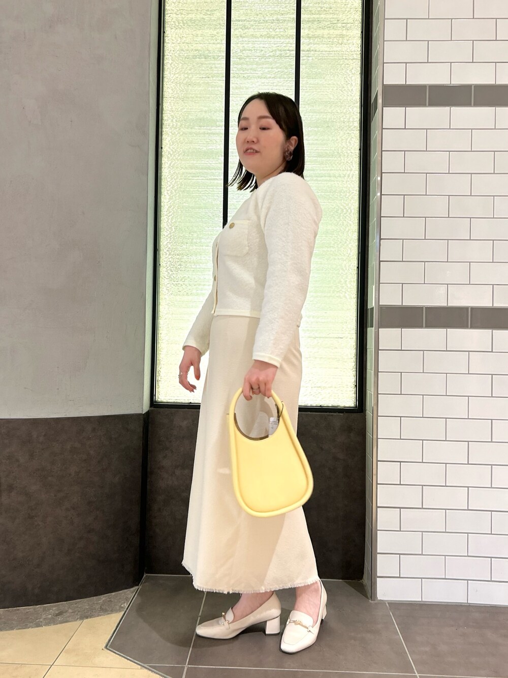 ホワイト系のカーディガン/ボレロ、ホワイト系のスカート、イエロー系のハンドバッグを着用したレディースの秋コーディネートの4枚目の写真