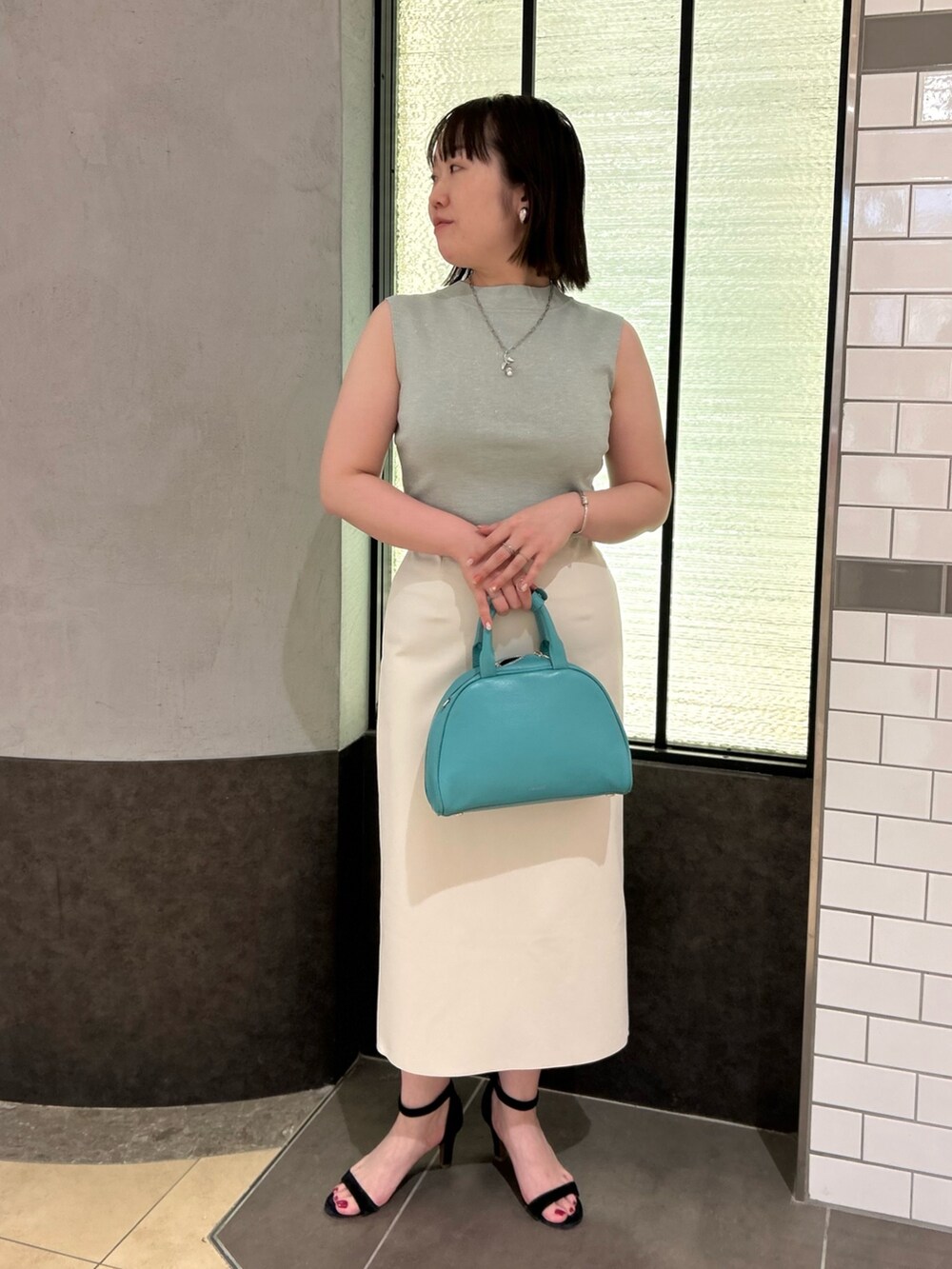 グリーン系のニット/セーター、ホワイト系のスカート、グリーン系のボストンバッグを着用したレディースの夏コーディネートの9枚目の写真
