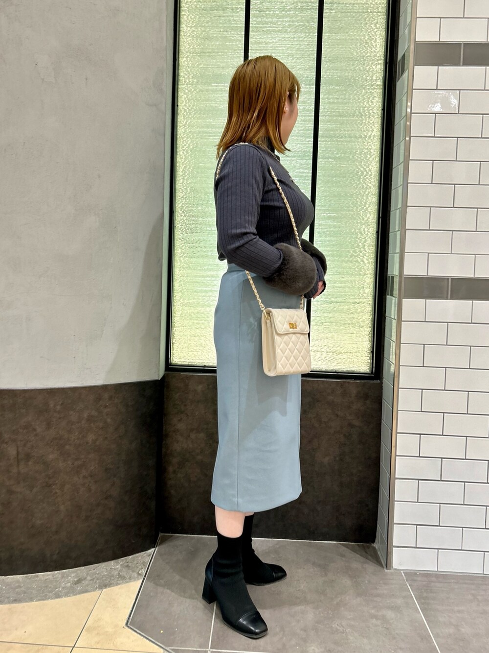 グレー系のニット/セーター、ブルー系のスカート、ホワイト系のショルダーバッグを着用したレディースの冬コーディネートの3枚目の写真