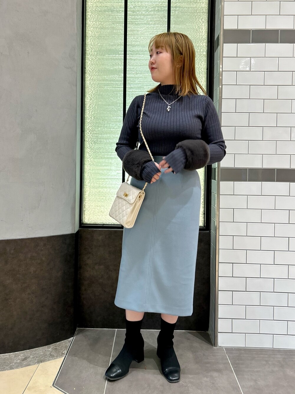 グレー系のニット/セーター、ブルー系のスカート、ホワイト系のショルダーバッグを着用したレディースの冬コーディネートの5枚目の写真