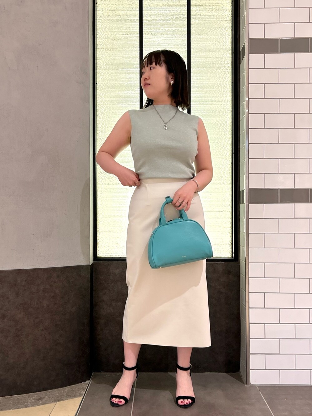 グリーン系のニット/セーター、ホワイト系のスカート、グリーン系のボストンバッグを着用したレディースの夏コーディネートの4枚目の写真