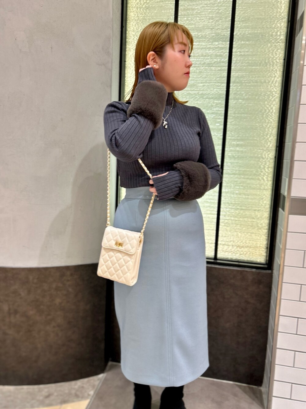 グレー系のニット/セーター、ブルー系のスカート、ホワイト系のショルダーバッグを着用したレディースの冬コーディネートの6枚目の写真