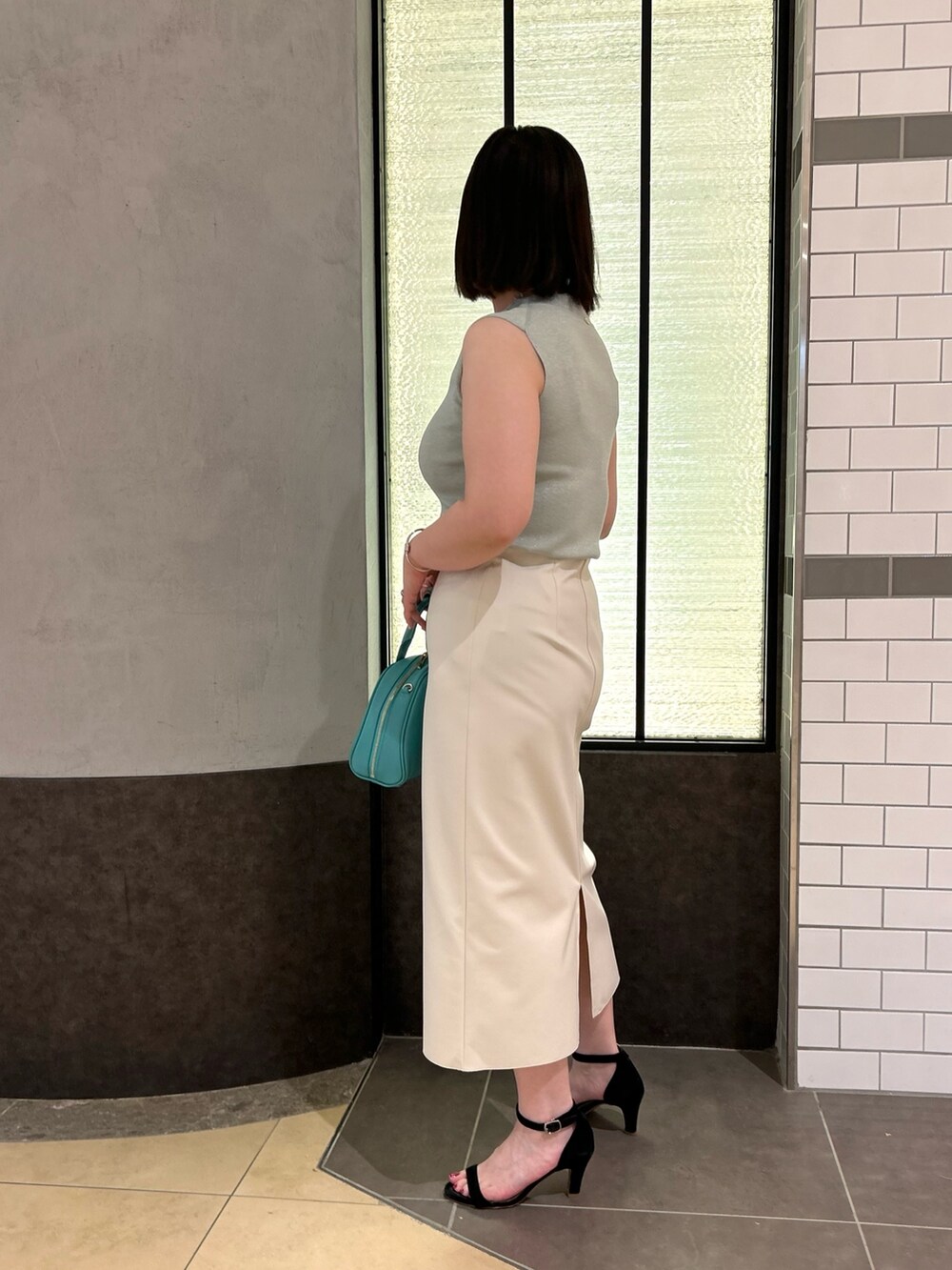 グリーン系のニット/セーター、ホワイト系のスカート、グリーン系のボストンバッグを着用したレディースの夏コーディネートの2枚目の写真