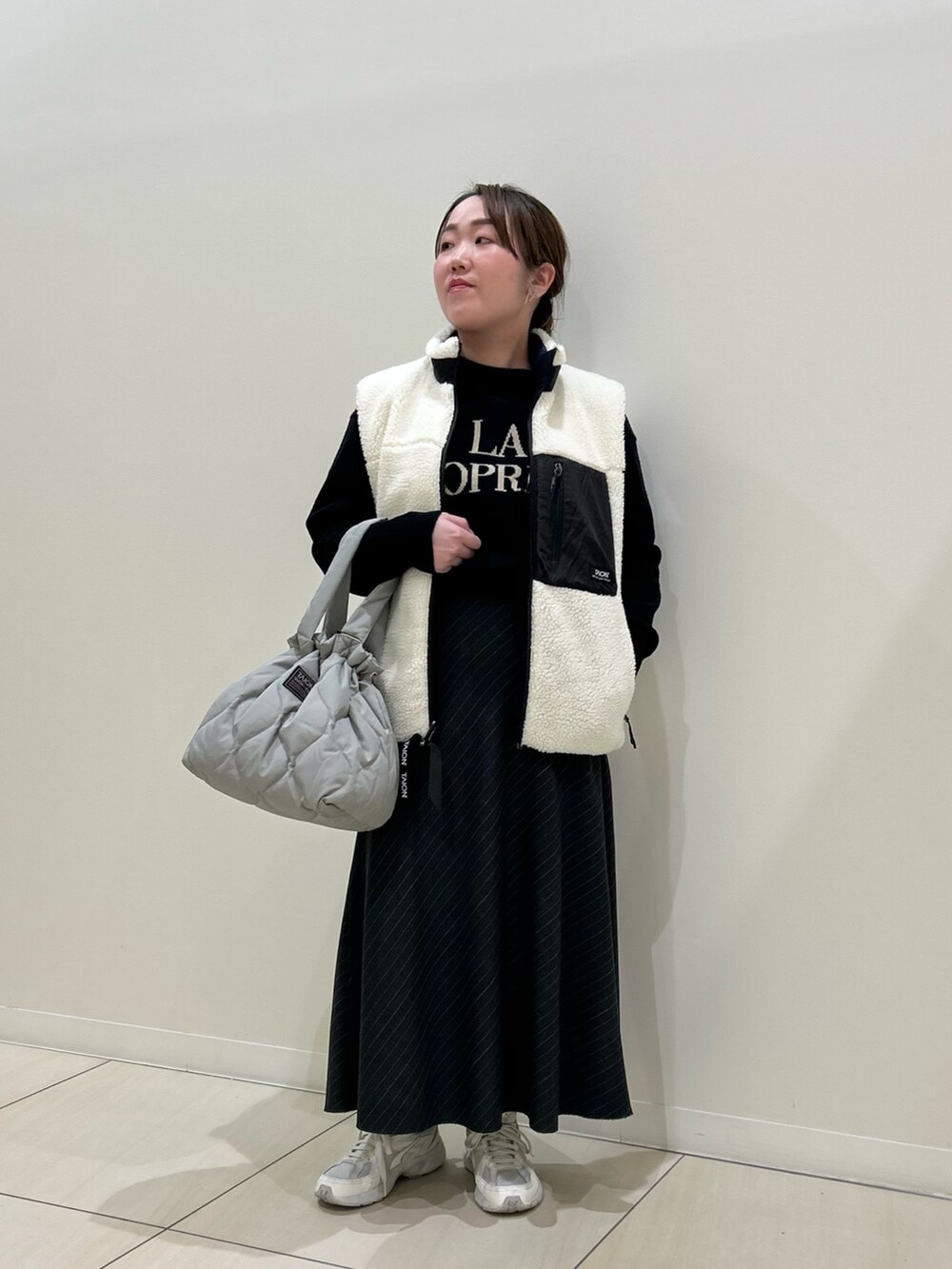 ホワイト系のダウンベスト、ブラック系のカーディガン/ボレロ、グリーン系のトートバッグを着用したレディースの冬コーディネートの6枚目の写真
