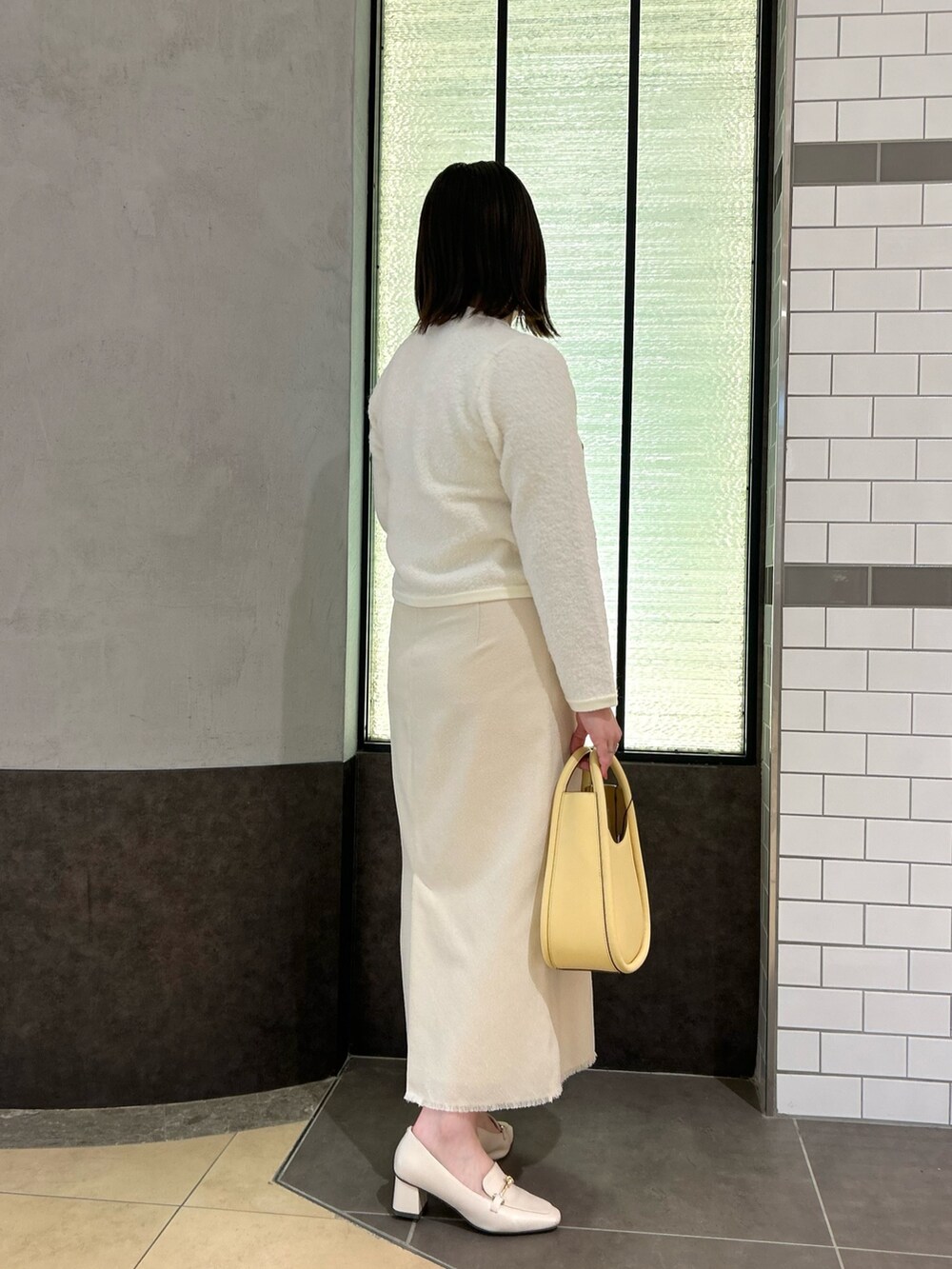 ホワイト系のカーディガン/ボレロ、ホワイト系のスカート、イエロー系のハンドバッグを着用したレディースの秋コーディネートの3枚目の写真