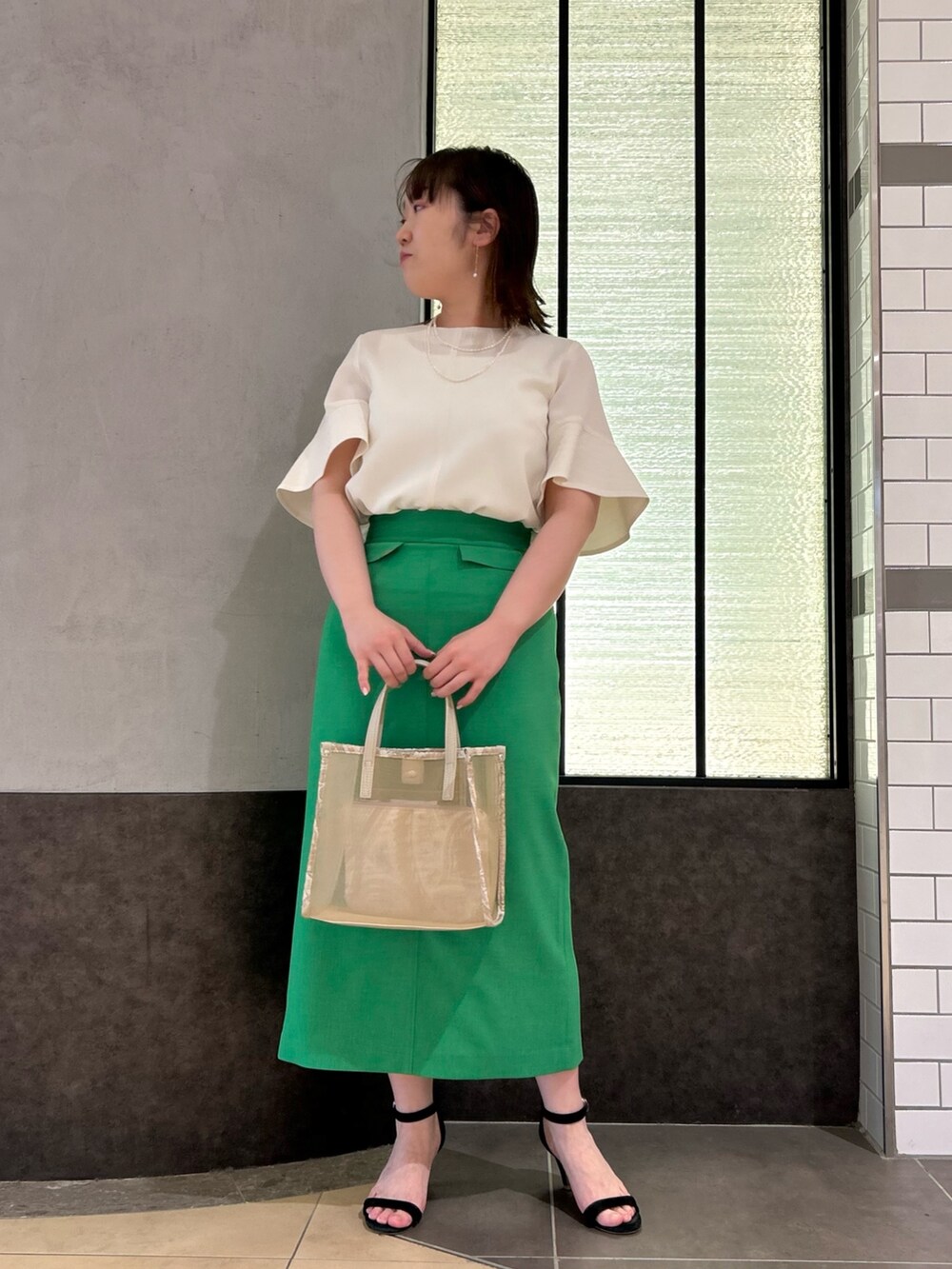 ベージュ系のトートバッグ、ホワイト系のシャツ/ブラウス、グリーン系のスカートを着用したレディースの春コーディネートの2枚目の写真