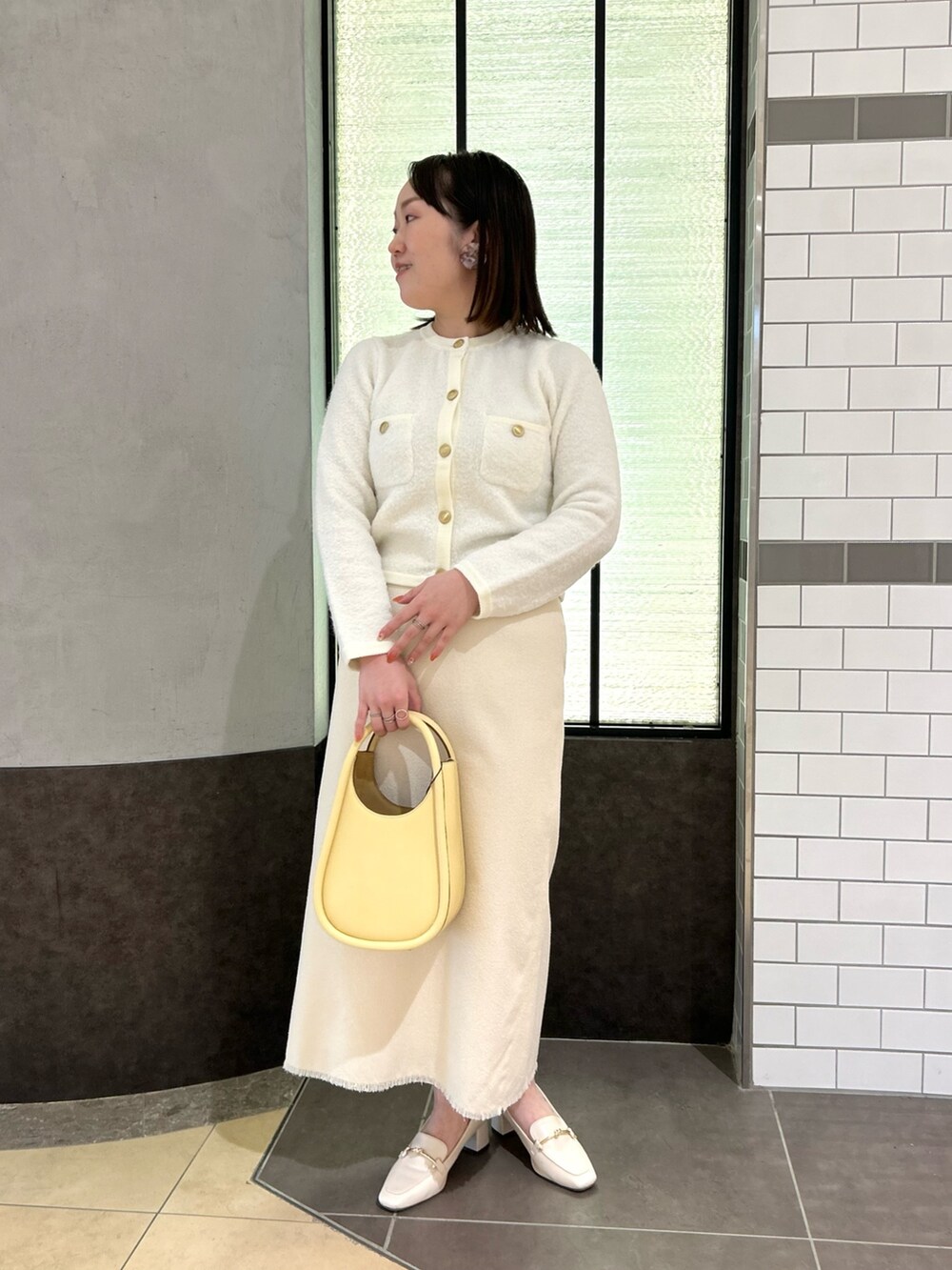 ホワイト系のカーディガン/ボレロ、ホワイト系のスカート、イエロー系のハンドバッグを着用したレディースの秋コーディネートの2枚目の写真