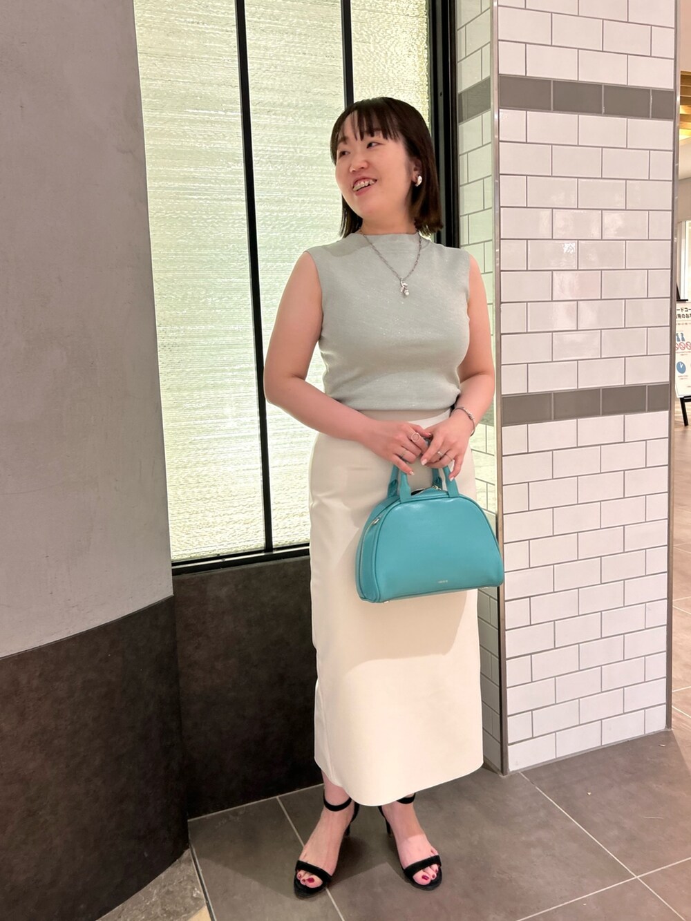 グリーン系のニット/セーター、ホワイト系のスカート、グリーン系のボストンバッグを着用したレディースの夏コーディネートの7枚目の写真