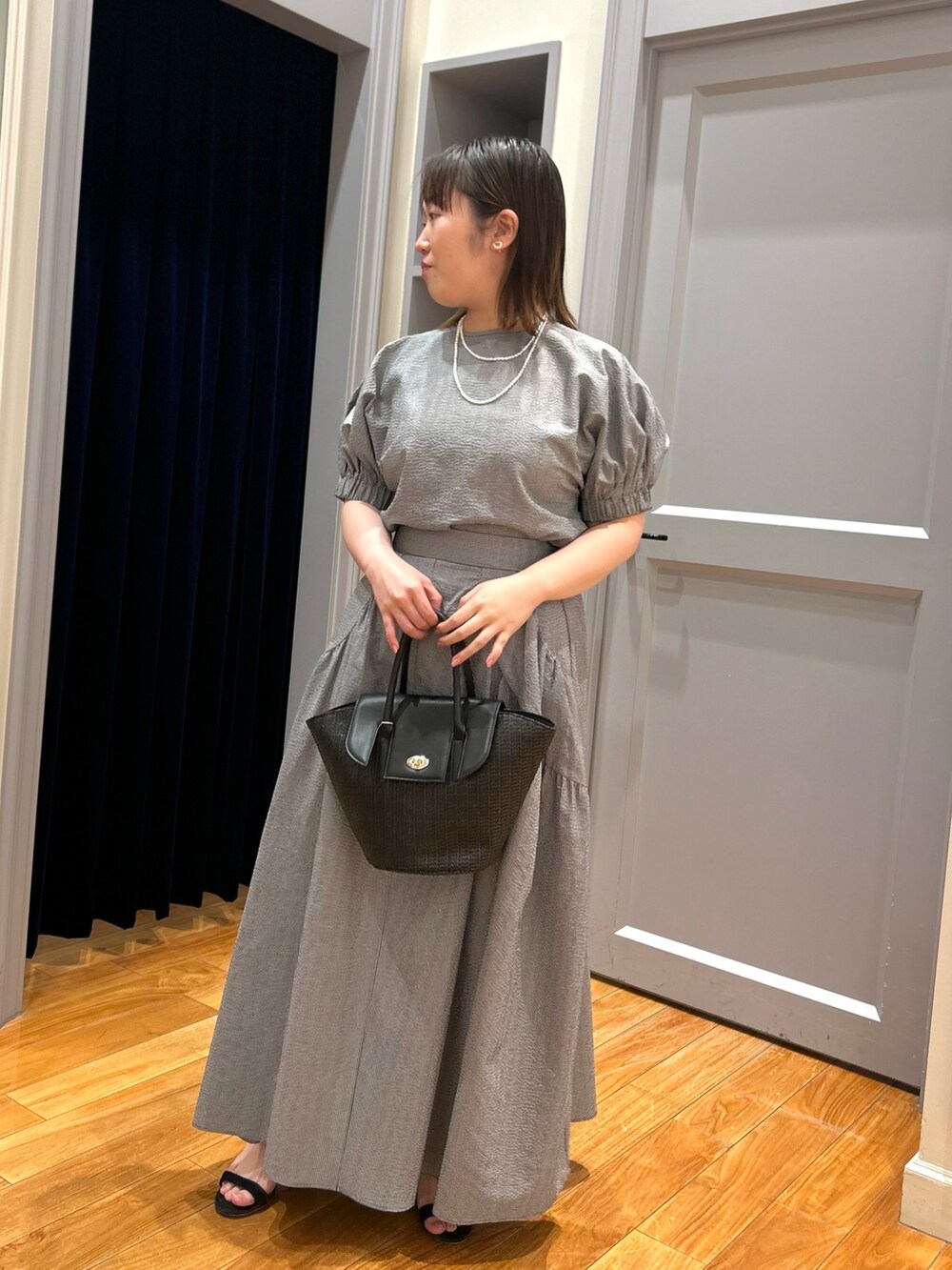 グレー系のシャツ/ブラウス、グレー系のスカート、ブラック系のかごバッグを着用したレディースの夏コーディネートの2枚目の写真