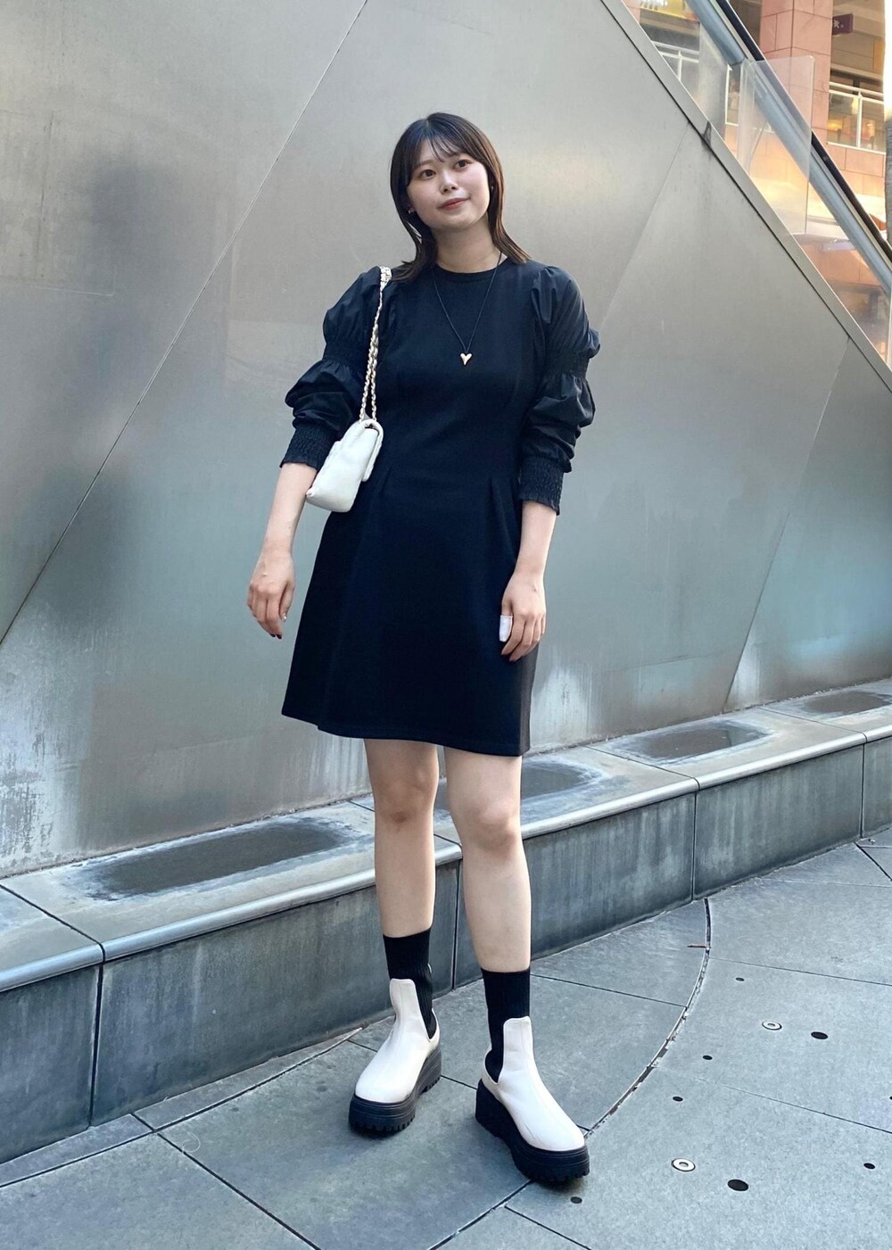 ホワイト系のショルダーバッグ、ホワイト系のブーツ、ブラック系のワンピースを着用したレディースの秋コーディネートの2枚目の写真