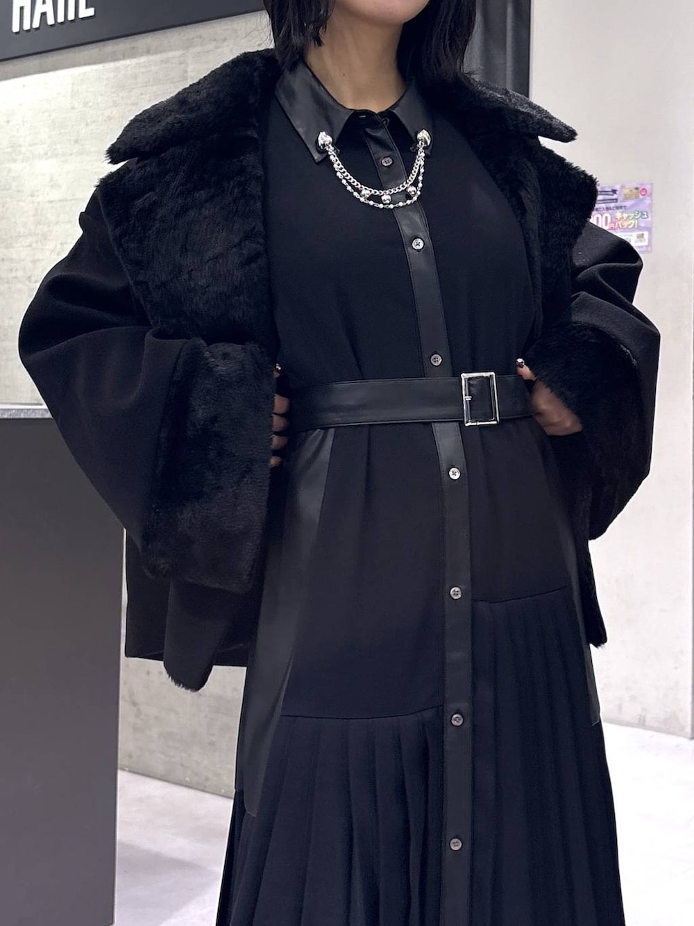 ブラック系のチェスターコート、ブラック系のブーツ、ブラック系のワンピースを着用したレディースの冬コーディネートの2枚目の写真