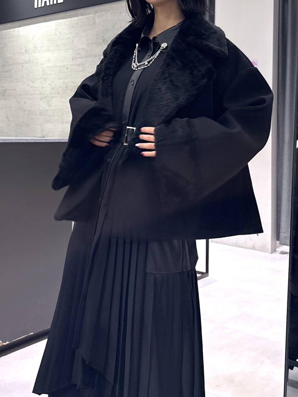 ブラック系のチェスターコート、ブラック系のブーツ、ブラック系のワンピースを着用したレディースの冬コーディネートの8枚目の写真