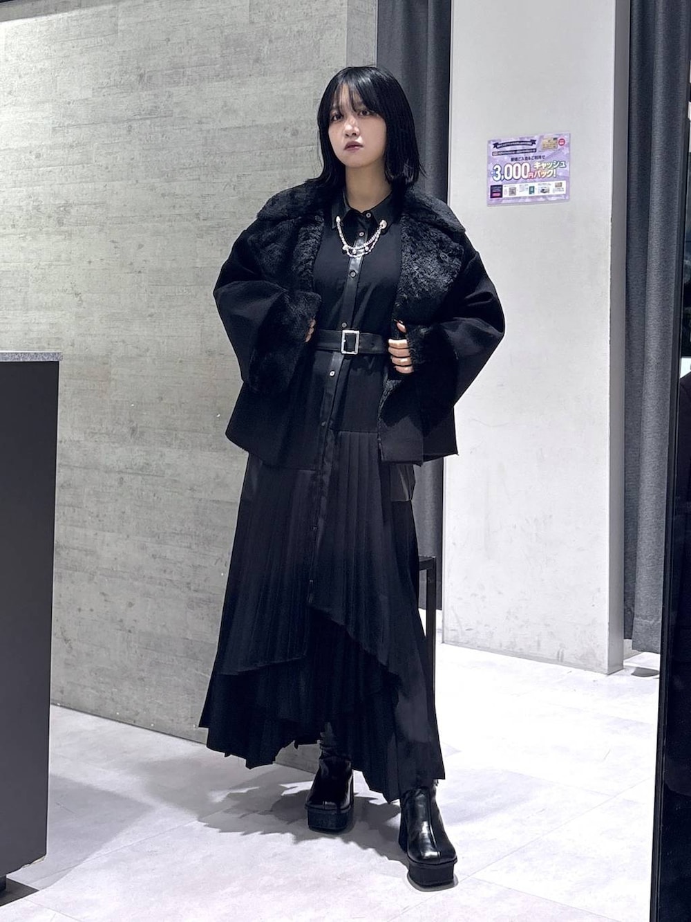 ブラック系のチェスターコート、ブラック系のブーツ、ブラック系のワンピースを着用したレディースの冬コーディネートの5枚目の写真