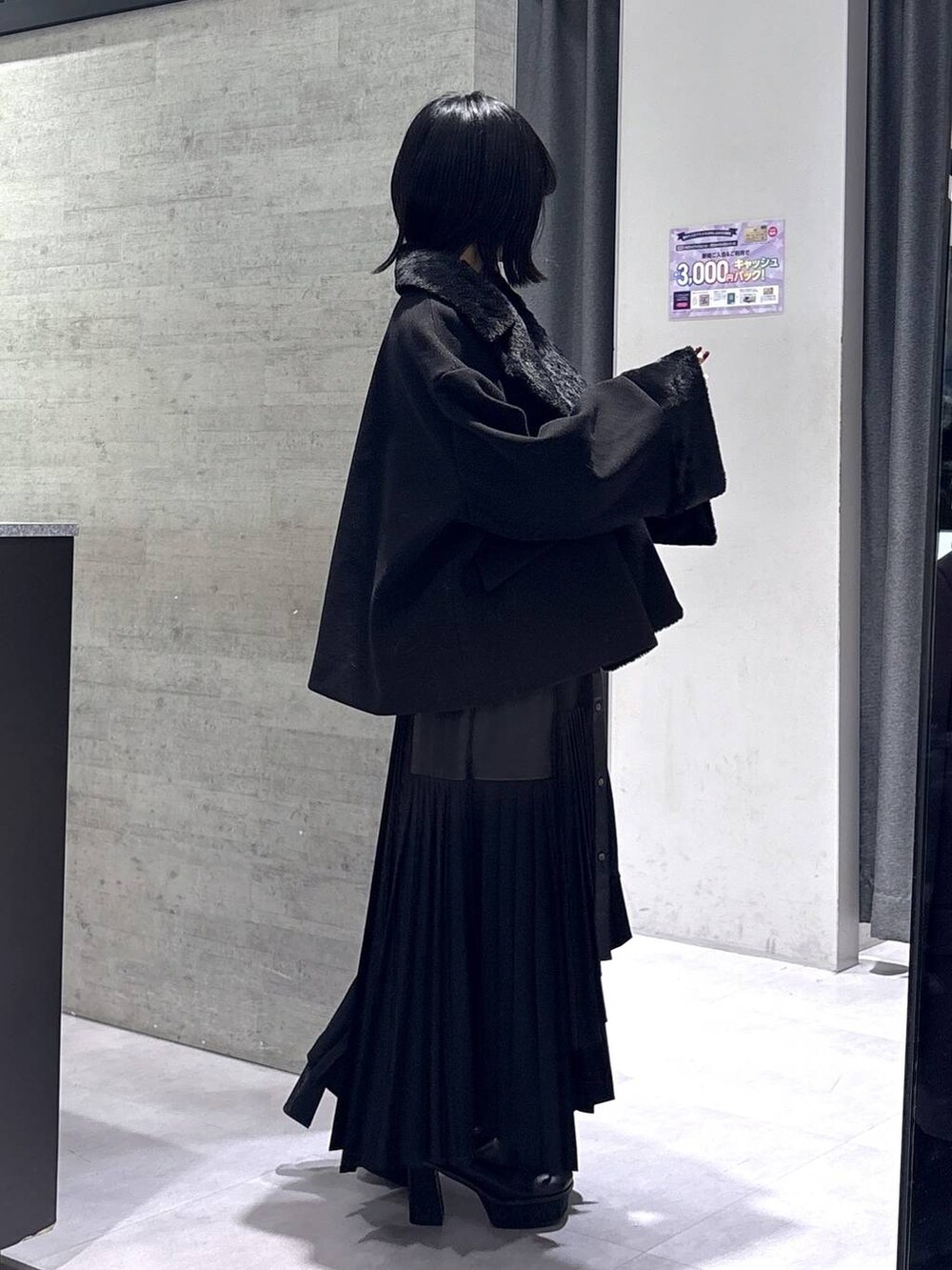 ブラック系のチェスターコート、ブラック系のブーツ、ブラック系のワンピースを着用したレディースの冬コーディネートの6枚目の写真